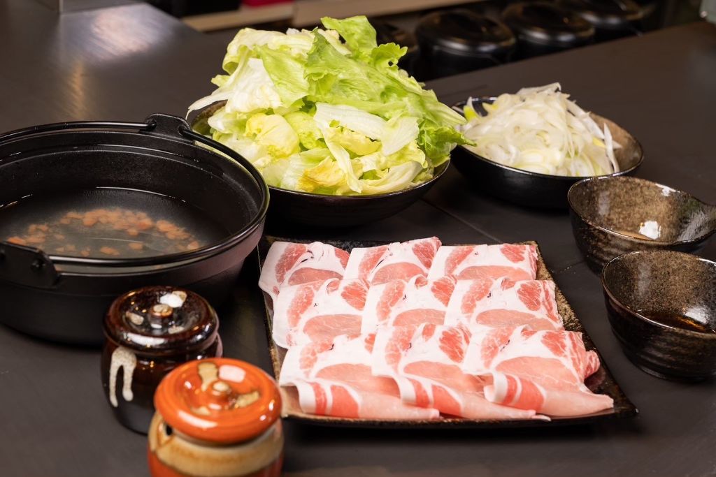 薄切りの豚肉を並べた皿と、ちぎったレタス、細切りにした長ねぎ、梅出汁を張った鍋