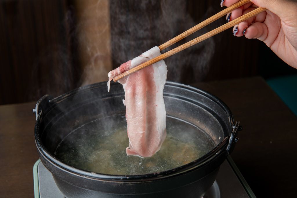 箸でつまんだ豚肉の薄切りを、湯気の立つ鍋の梅出汁にくぐらせているところ